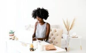 blog post checklist woman working on a laptop on a white desk with office accessories and a cream chair