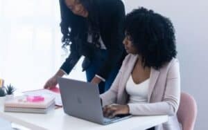 women working on a laptop with notebooks on table