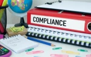 desk with stack of notebooks and red one with compliance